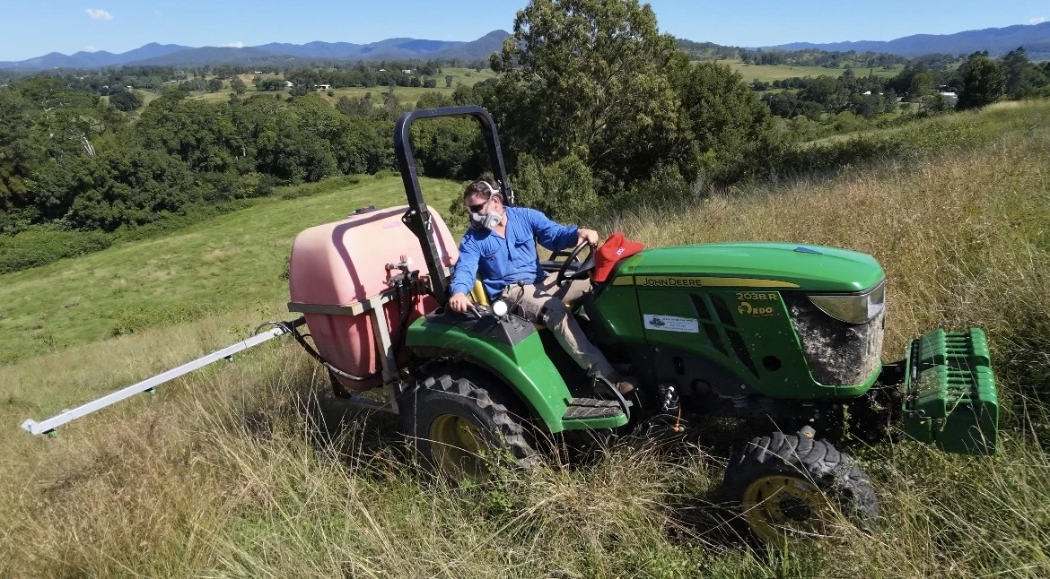 James operating his John Deere tractor and boom sprayer in a hillside paddock